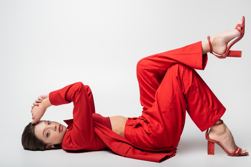 longitud completa de la mujer joven de moda en traje rojo acostado en gris - Foto, imagen