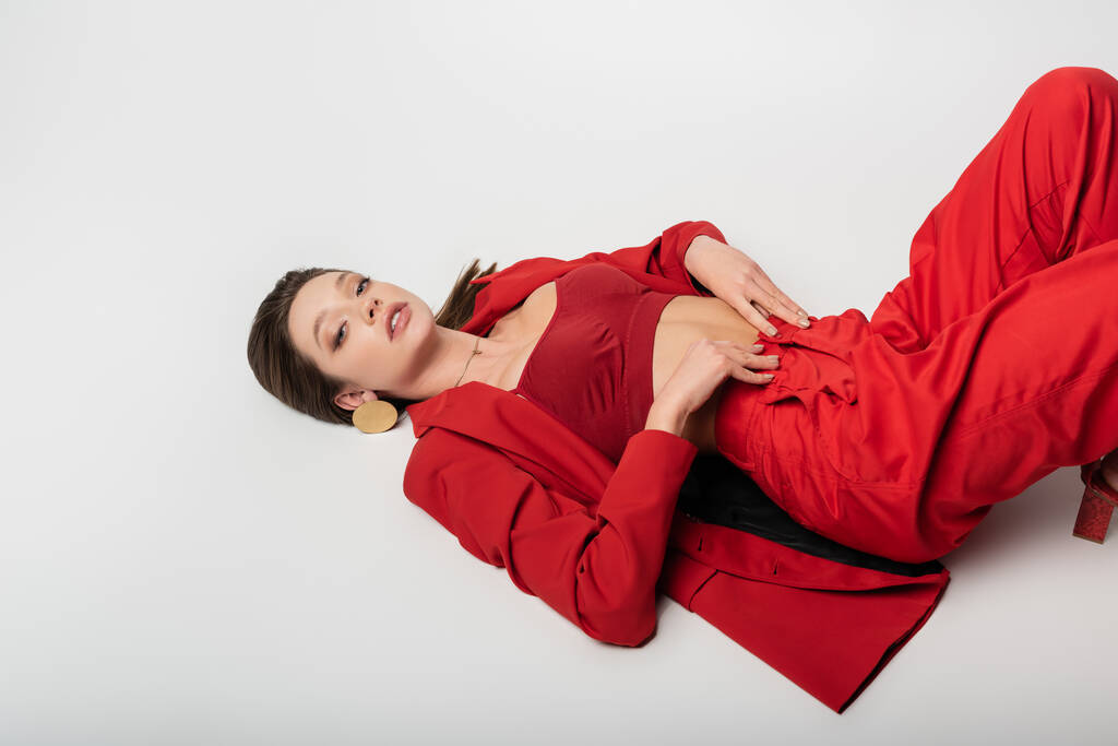 high angle view of trendy young woman in red outfit lying on grey - Photo, Image