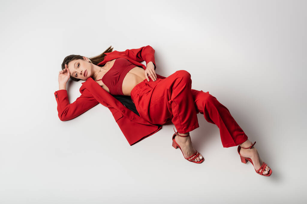 vysoký úhel pohledu stylové mladé ženy v červené oblečení ležící na šedé - Fotografie, Obrázek