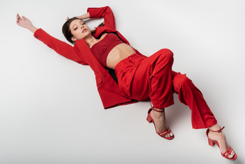 Hochwinkelaufnahme des stylischen jungen Modells in rotem Outfit und Schuhen, die auf grau liegen - Foto, Bild