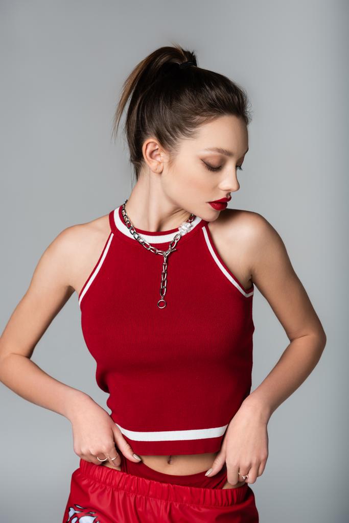 junge stylische Frau in rotem sportlichem Outfit und Halskette isoliert auf grau - Foto, Bild