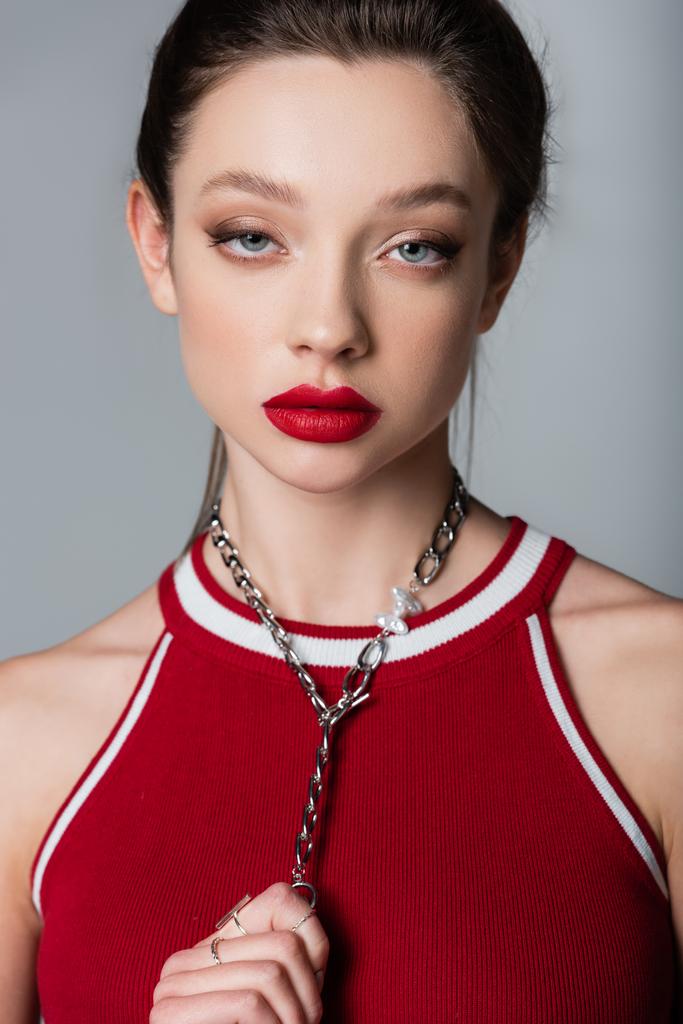 young pretty woman with red lips pulling necklace chain isolated on grey - Photo, Image