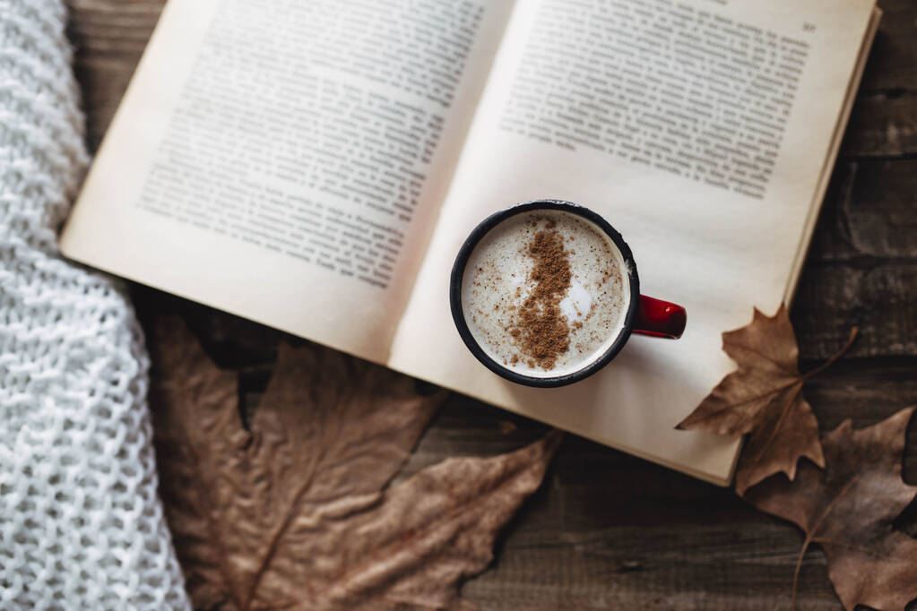 Πρωινή ρουτίνα. Καφές με mil κακάο και κανέλα. Διαβάζω ένα βιβλίο το φθινόπωρο. Ξύλινο τραπέζι με φθινοπωρινά φύλλα. - Φωτογραφία, εικόνα
