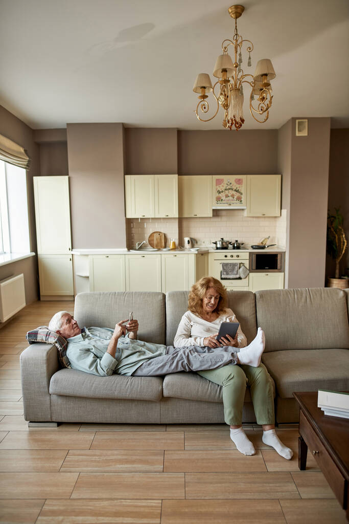 Couple utilisant des gadgets tout en se reposant sur le canapé à la maison - Photo, image