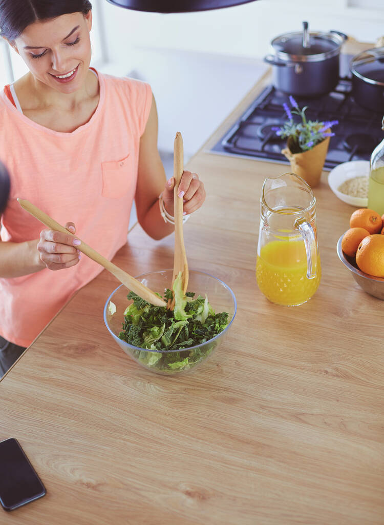 Lächelnde junge Frau mixt frischen Salat in der Küche. - Foto, Bild