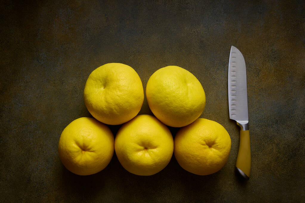 5 large yellow ripe Sweetie or Pomelite and chefs knife on dark background, top view, close-up - Photo, Image