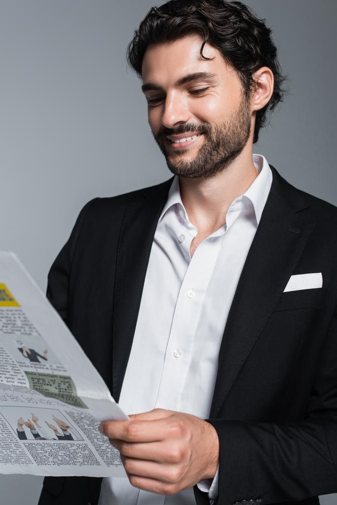 felice uomo d'affari bruna in blazer nero leggere giornale isolato su grigio - Foto, immagini