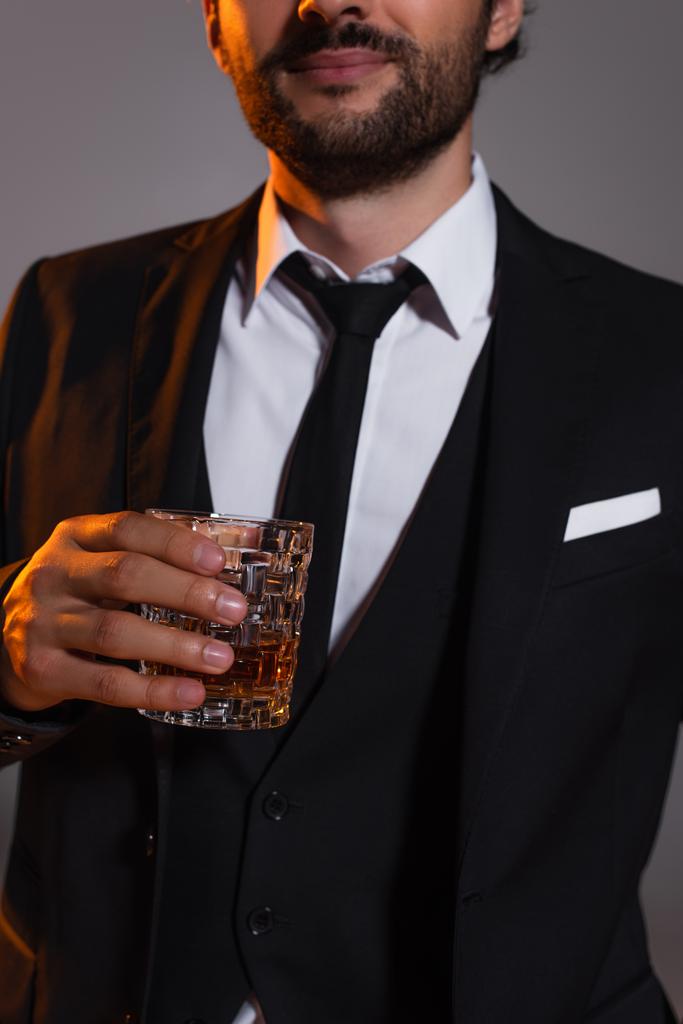 灰色で隔絶されたウイスキーのグラスを手にしたエレガントなフォーマルウェア姿で男を切り取る - 写真・画像