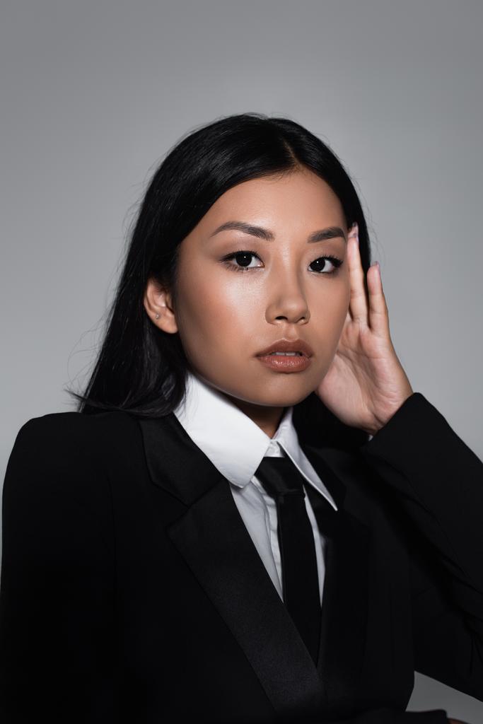 barna ázsiai nő fekete blézer és nyakkendő nézi kamera elszigetelt szürke - Fotó, kép