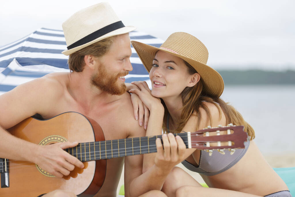 ボーイフレンドがビーチでギターを弾く - 写真・画像