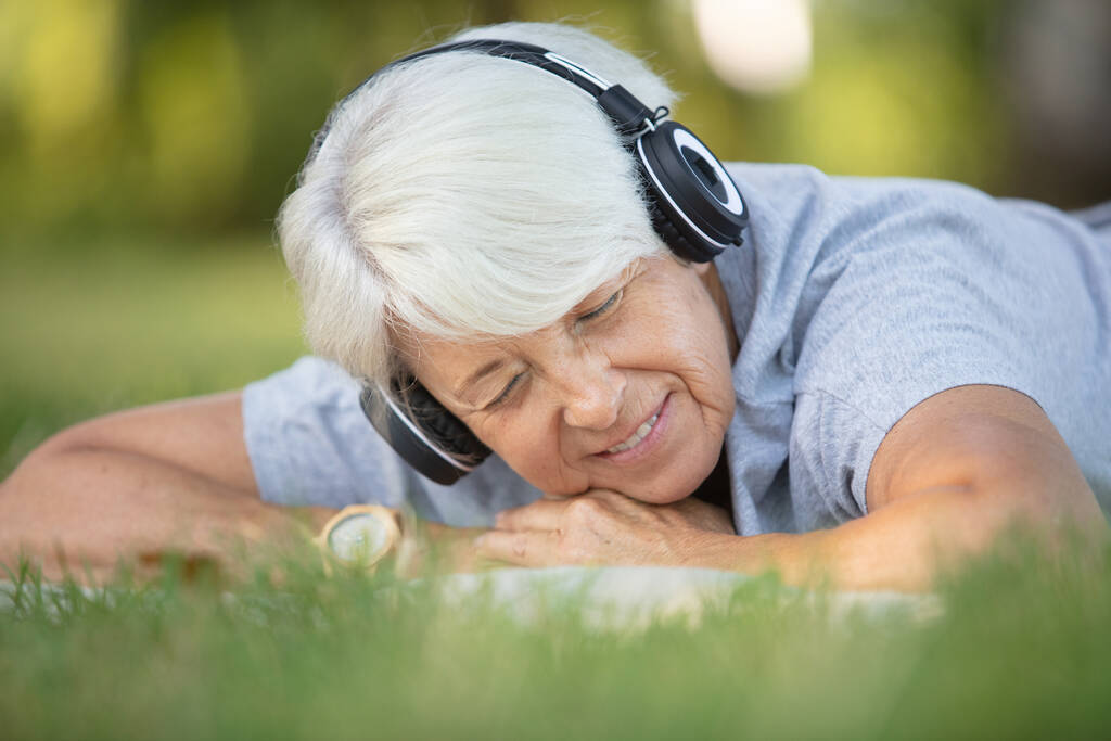 gelukkig ouder vrouw luistert naar muziek in een park - Foto, afbeelding