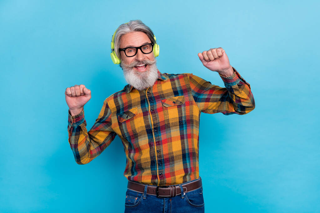 Zdjęcie szczęśliwego emeryta nosić okulary koszuli kratę ciesząc się muzyką taniec pięści odizolowany niebieski kolor tła - Zdjęcie, obraz