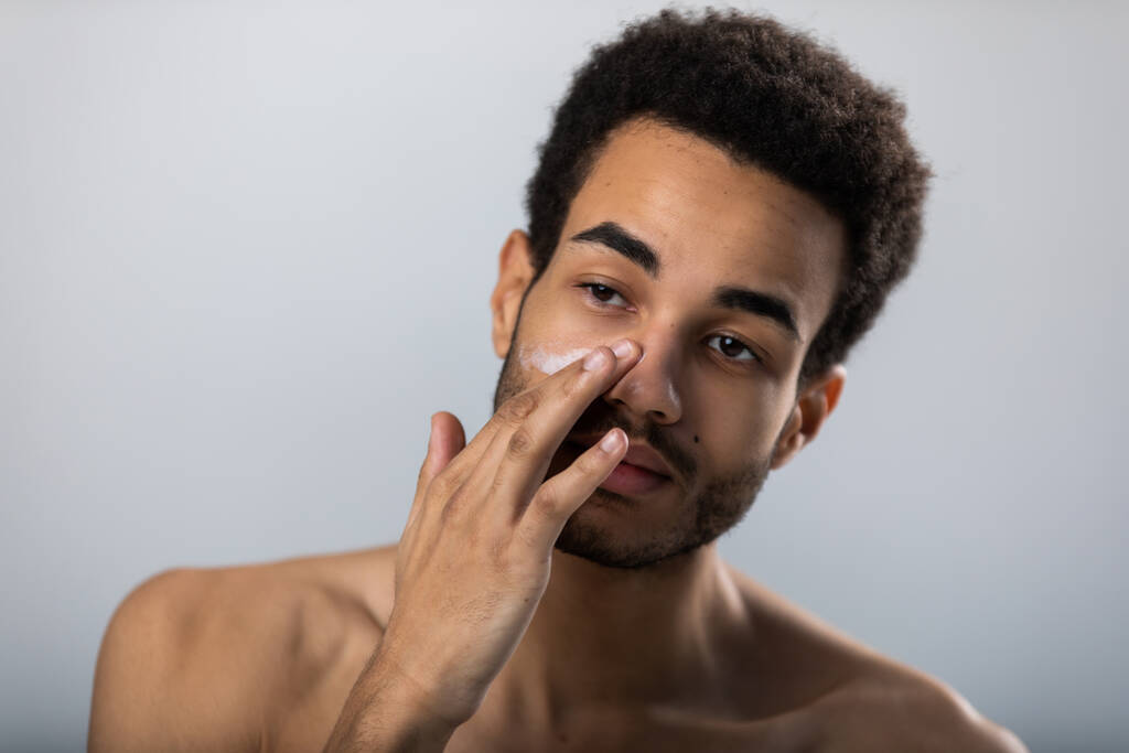 A fiatal afro-amerikai férfi hidratáló krémet tesz az arcára. Férfi bőrápolás. - Fotó, kép