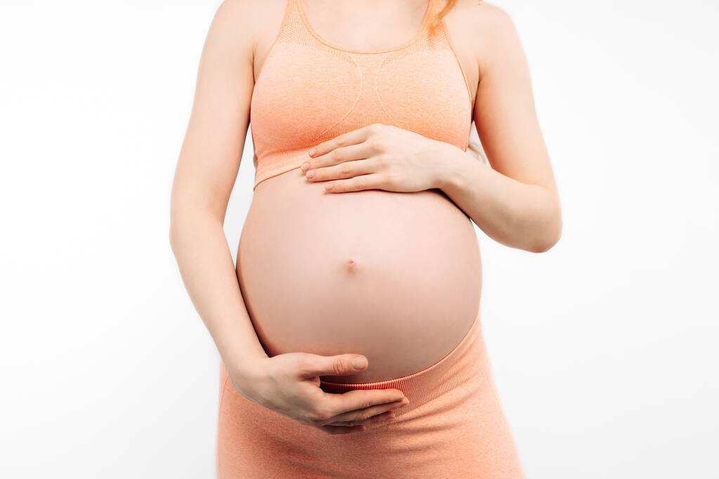 Schwangere hält ihre Hände auf dem Bauch vor weißem Hintergrund. Schwangerschaft, Mutterschaft, Vorbereitung und Erwartung Konzept. Nahaufnahme, Schöne zarte Stimmung Foto der Schwangerschaft. - Foto, Bild