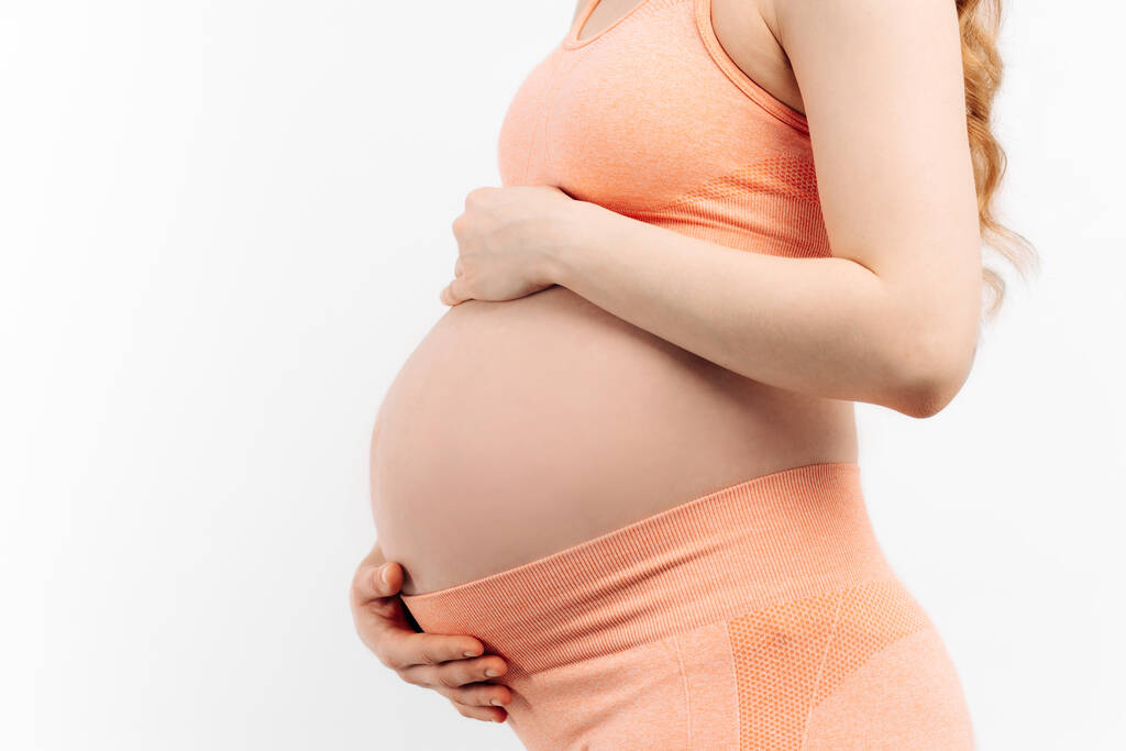 Крупный план беременной женщины, трогающей живот на белом фоне. Женщина ждет ребенка, счастливая беременная женщина с большим животом. Концепция беременности, материнства, подготовки и ожидания - Фото, изображение