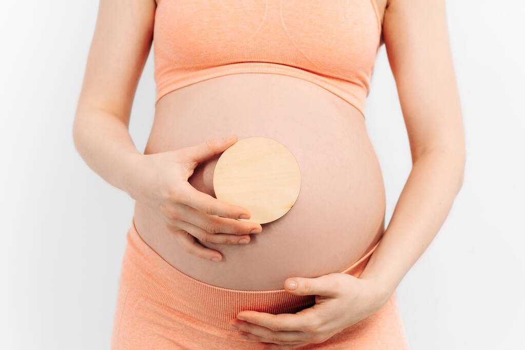 A terhes nő a hasán tartja a kezét, fehér alapon. Terhesség, anyaság, felkészülés és elvárás koncepció. Közelkép, Gyönyörű gyengéd hangulatú fotó a terhességről. - Fotó, kép