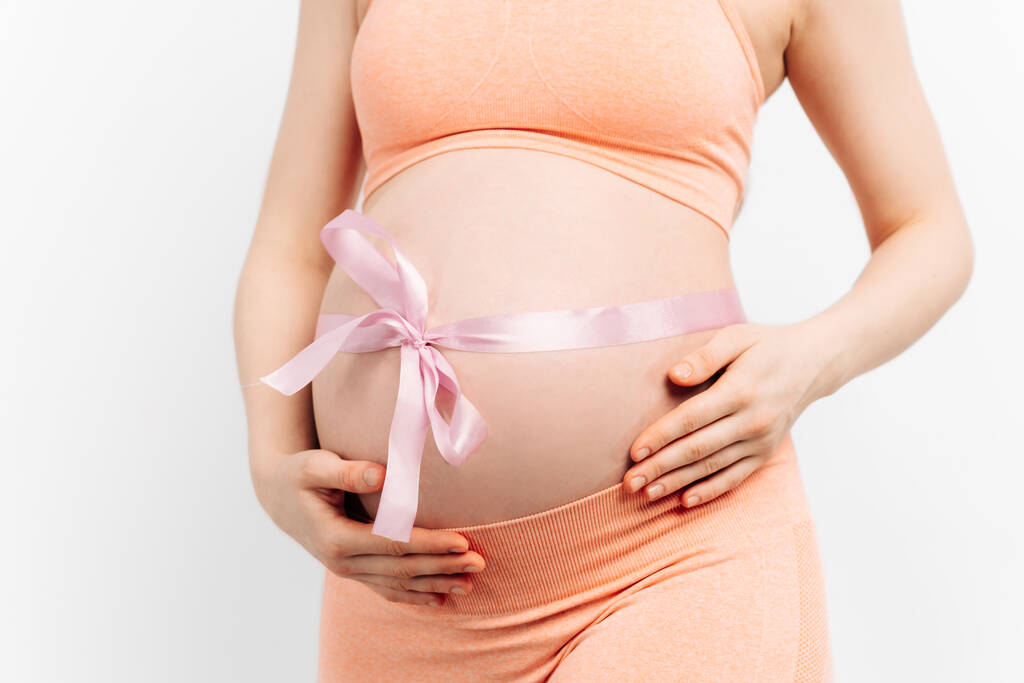 вагітна жінка зі стрічкою на животі торкається її живота. Жінка очікує на дитину, щаслива вагітна жінка з великим животом. Поняття вагітності, материнства, підготовки та очікування
 - Фото, зображення
