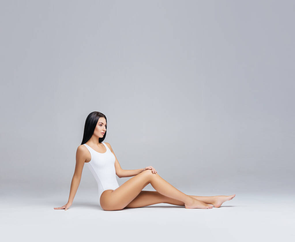 Aantrekkelijk en slank brunette meisje in wit ondergoed poseren in de studio. Gezond levensstijl, sport en lichaamsverzorging concept. - Foto, afbeelding