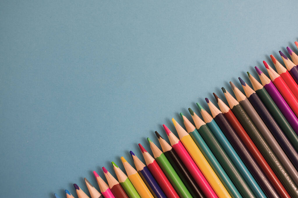 Close-up van gekleurde potloden geplaatst op blauwe papieren achtergrond met kopieerruimte voor uw afbeelding of tekst. Hoge kwaliteit foto - Foto, afbeelding
