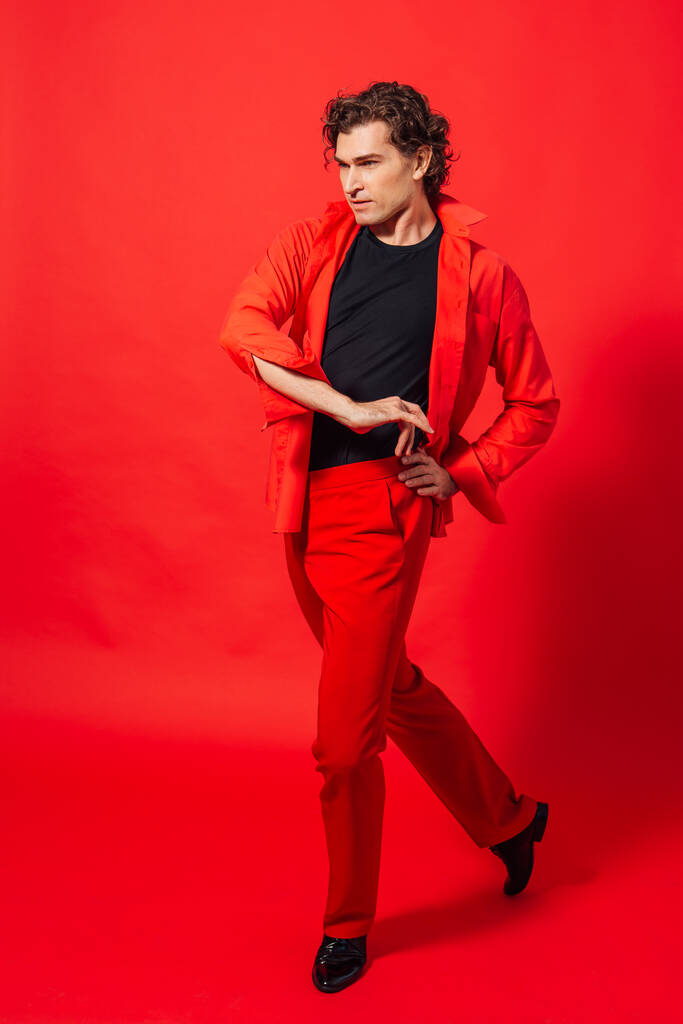 Portrait of a tall handsome man dressed in red shirt posing on the red background. - Photo, Image