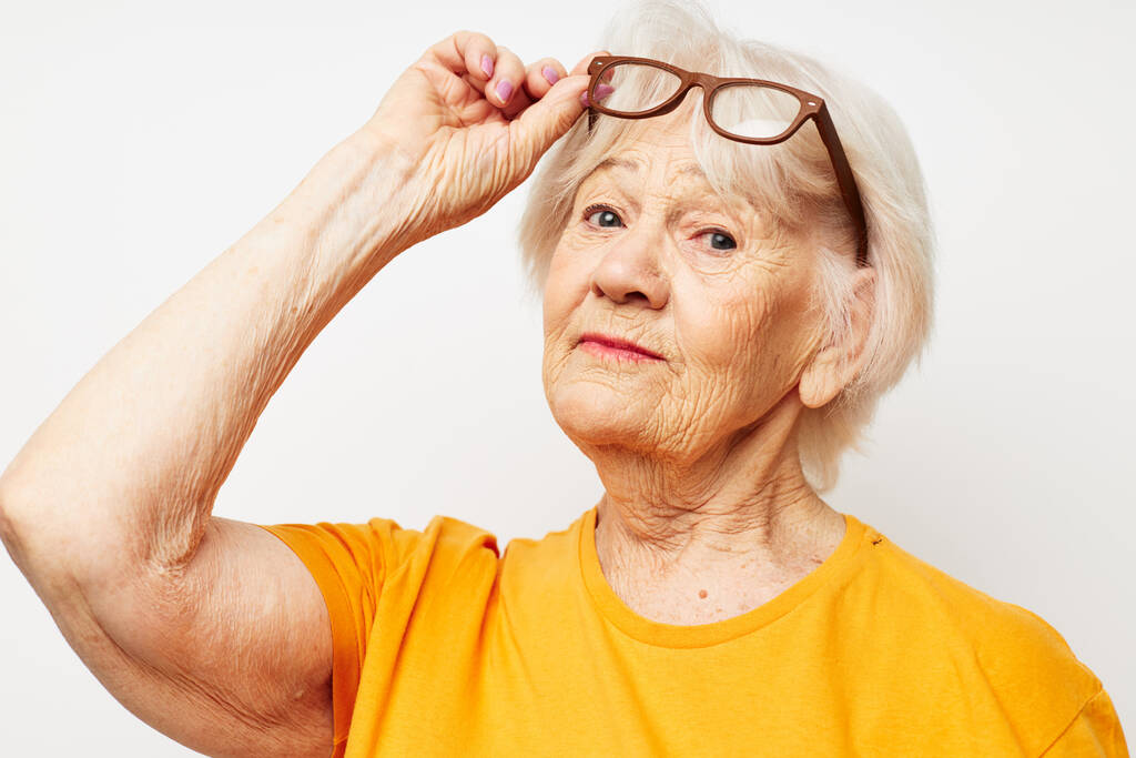 emocjonalna starsza kobieta w luźnej koszulce i okularach lekkie tło - Zdjęcie, obraz