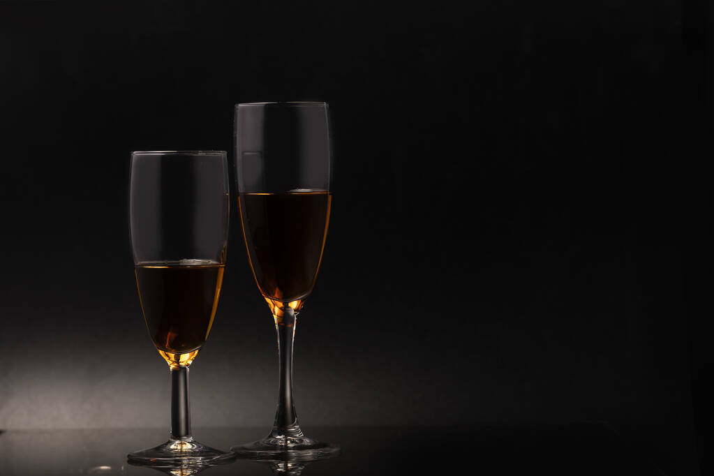 Dvě sklenice různých velikostí s alkoholickým nápojem na černém pozadí. - Fotografie, Obrázek