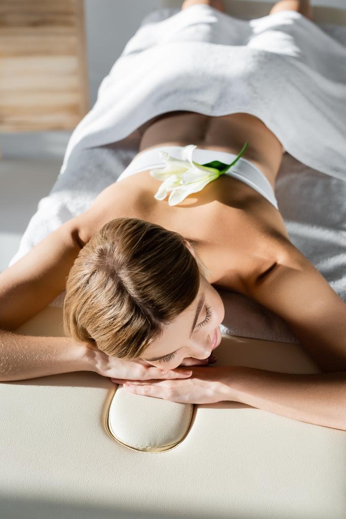 fiore sul retro della donna bionda sdraiata sul tavolo da massaggio  - Foto, immagini