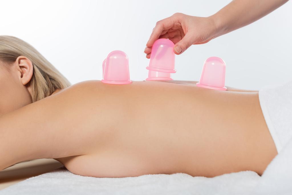 cropped view of masseuse putting pink massage cups on back of cheerful client isolated on white - Photo, Image