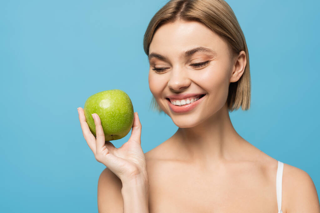 Χαρούμενη νεαρή γυναίκα που κρατά ώριμο πράσινο μήλο απομονωμένο στο μπλε  - Φωτογραφία, εικόνα