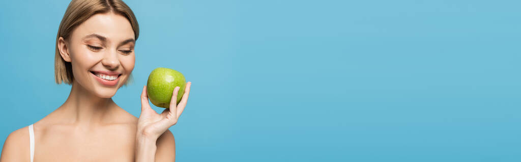 jovem alegre segurando maçã verde madura isolado em azul, banner - Foto, Imagem