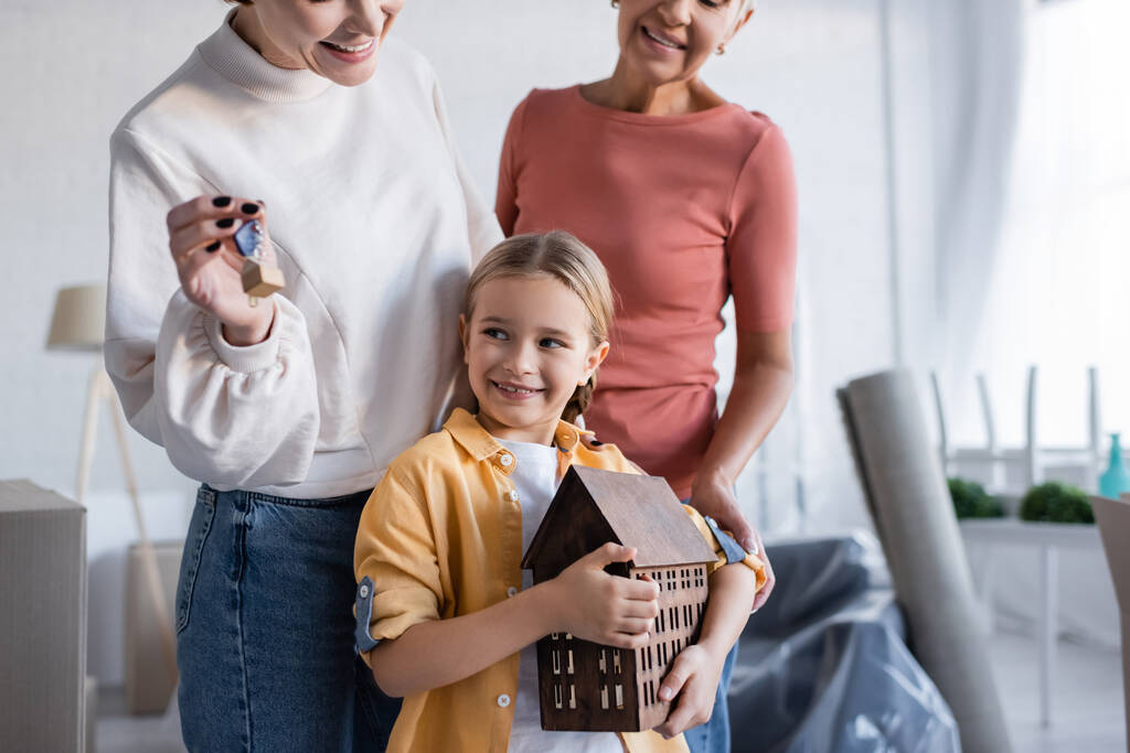 cheerful girl holding house model near same sex parents with key from new apartment - Photo, Image