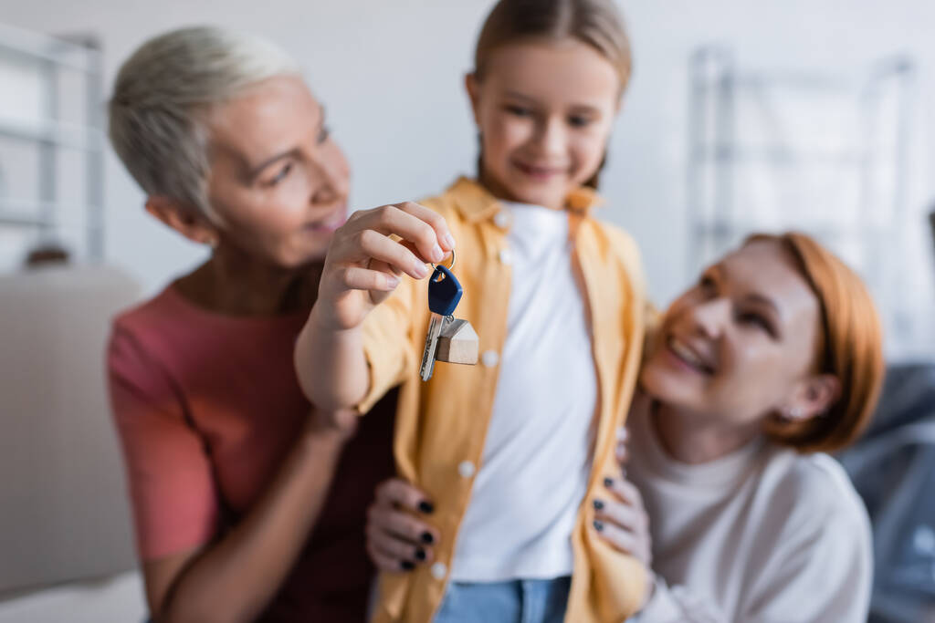 blurred girl holding key from new apartment near same sex parents - Photo, Image