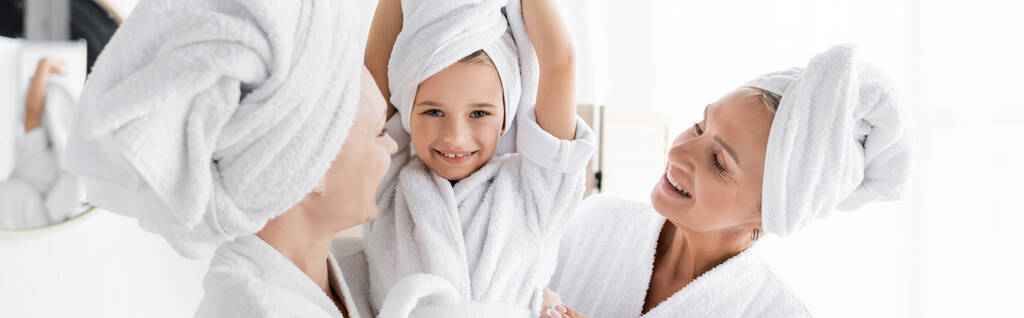 Uśmiechnięta dziewczyna w ręczniku patrząca w kamerę obok matek w domu, sztandar  - Zdjęcie, obraz