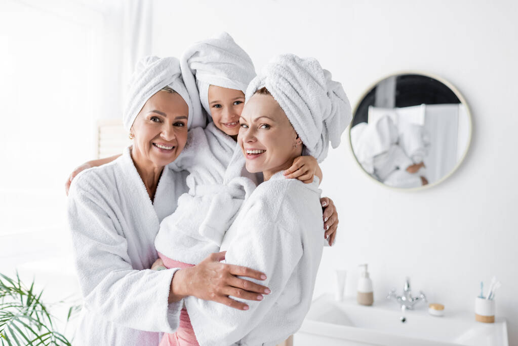 Positives lesbiennes mères tenant enfant en peignoir dans la salle de bain  - Photo, image