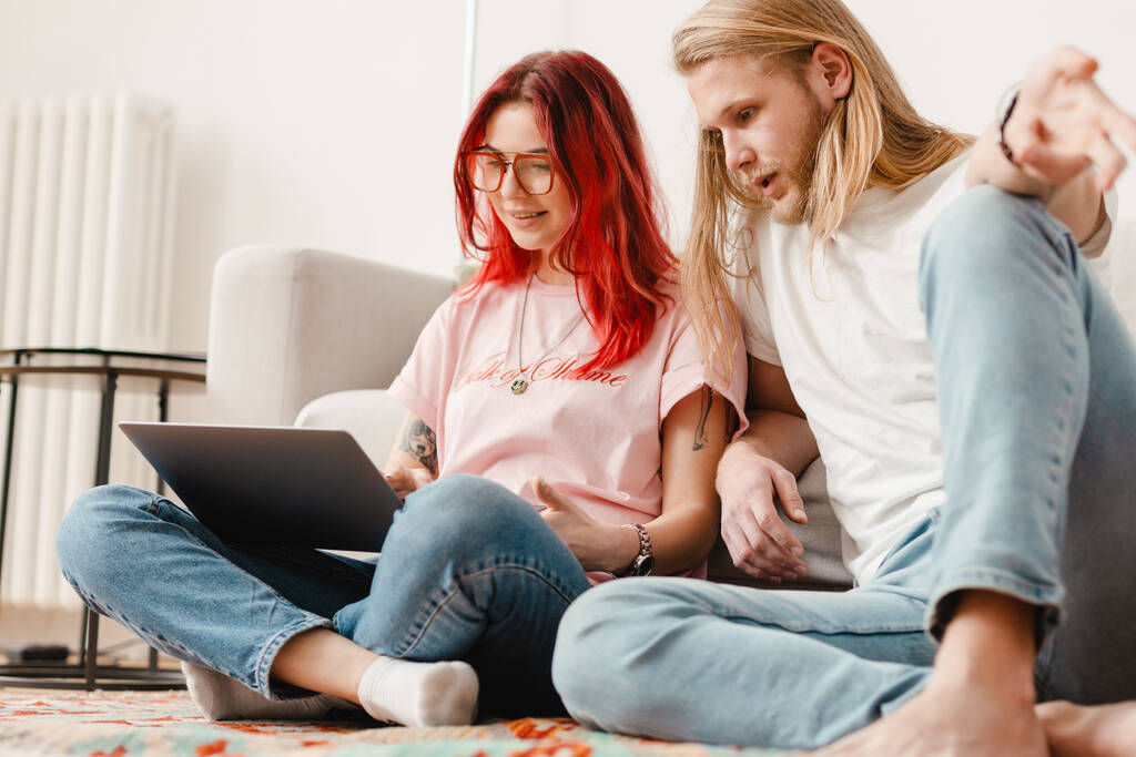 Weißer Mann und Frau benutzen Laptop zusammen, während sie zu Hause auf dem Boden sitzen - Foto, Bild