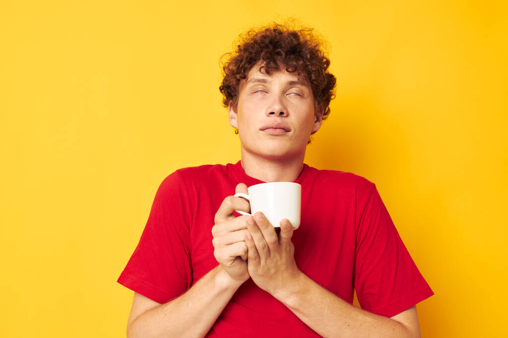 Nuori kiharatukkainen mies valkoinen muki käsissä juoman eristetty tausta muuttamaton - Valokuva, kuva