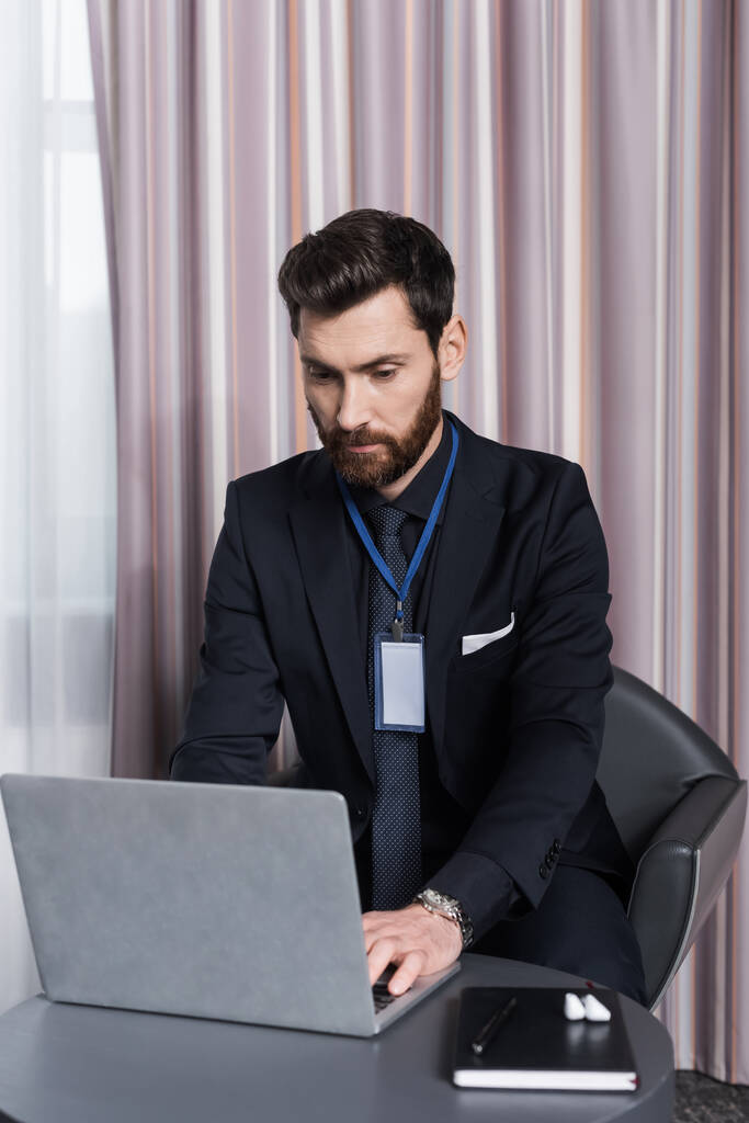 bearded businessman with id badge using laptop in hotel room - Photo, Image
