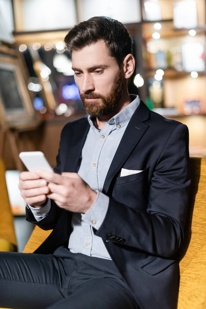 бородатий чоловік у костюмі, використовуючи мобільний телефон у фойє готелю
   - Фото, зображення