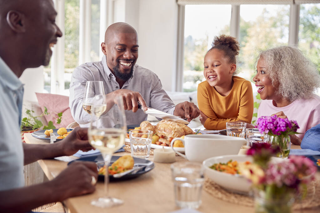 Vader snijden als multi generatie familie zitten rond de tafel thuis en genieten van het eten van maaltijd - Foto, afbeelding