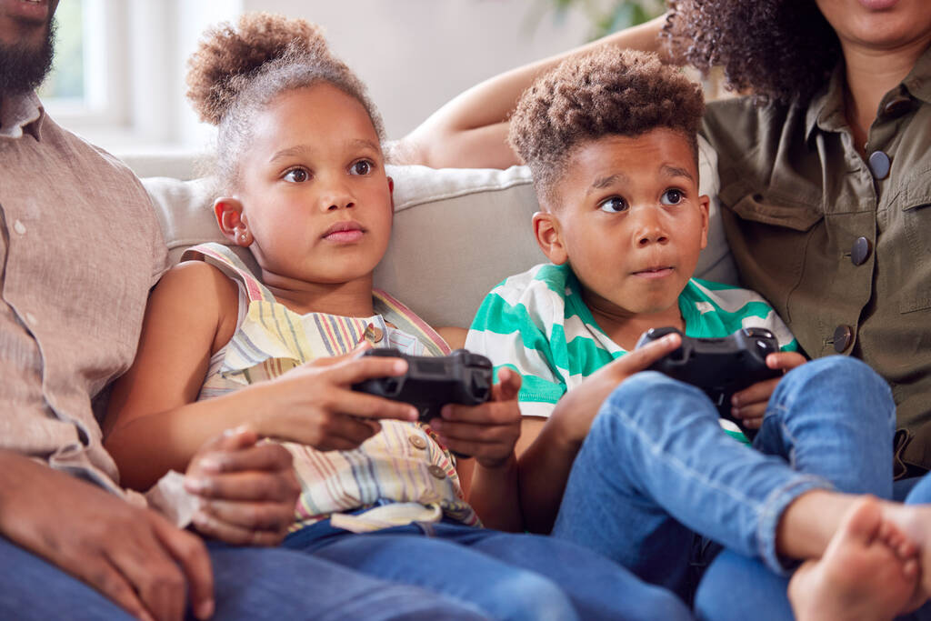 Ouders zitten op de bank met kinderen thuis het spelen van videospel samen - Foto, afbeelding