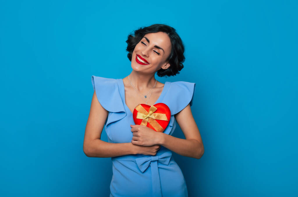 Women's day. St. Valentine's day. Birthday. Holidays. Close up portrait of elegant excited happy woman in dress with gift box in hands isolated on blue background - Photo, Image