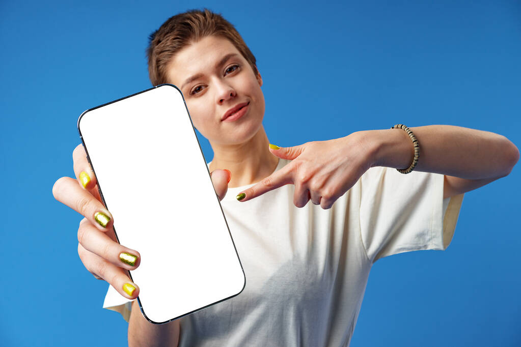 Portret van een jonge vrouw tonen blanco scherm mobiele telefoon terwijl staande over blauwe achtergrond - Foto, afbeelding