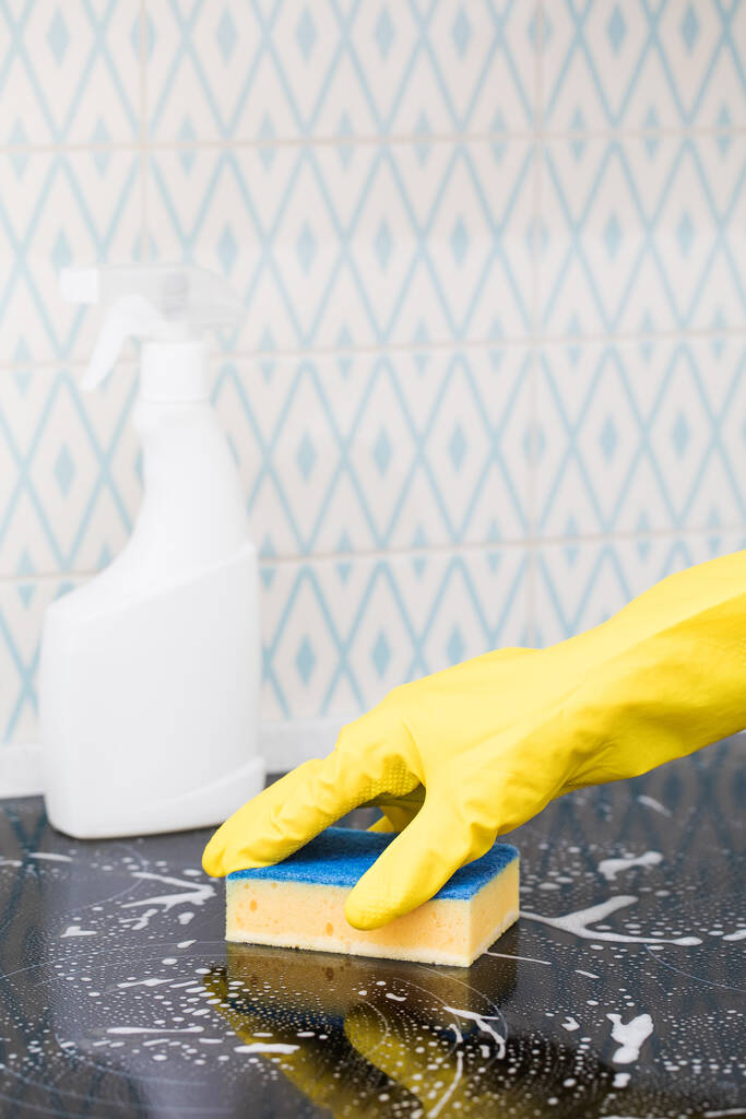 Eine Putzfrau in einem gelben Handschuh wäscht einen Küchenherd mit Schwamm und Schaum. Weiße Küchenreiniger-Attrappe.  - Foto, Bild