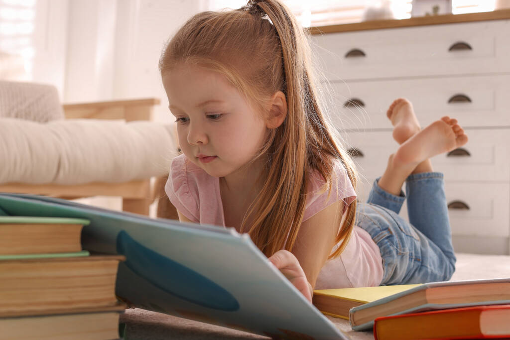 Evde yerde kitap okuyan tatlı küçük bir kız. - Fotoğraf, Görsel