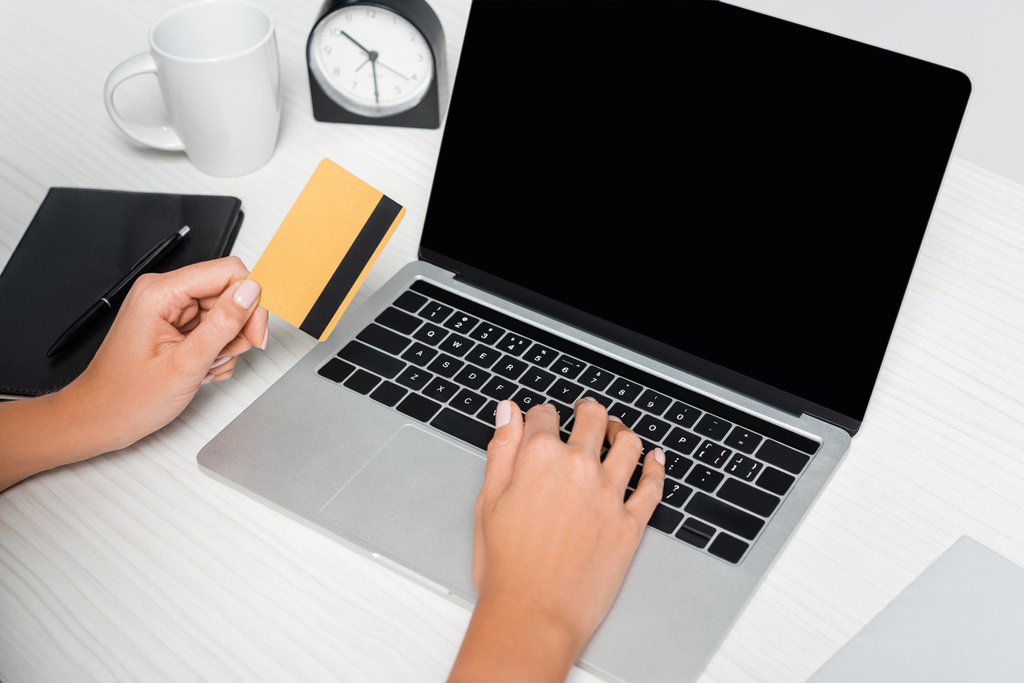 vista cortada de mulher segurando cartão de crédito perto de laptop com tela em branco e notebook na mesa branca - Foto, Imagem