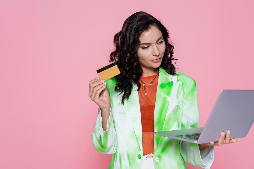 брюнетка жінка в блістері тримає кредитну картку і ноутбук ізольовані на рожевому
  - Фото, зображення