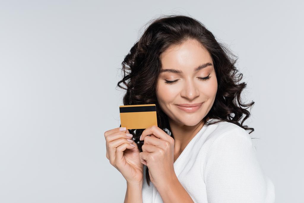 pleased young woman holding credit card isolated on grey - Photo, Image