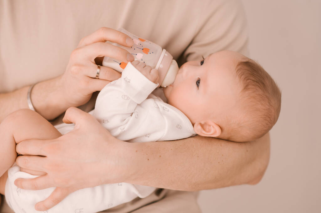 Caucasian father feeds newborn baby girl from a bottle. Parent holding rocking child daughter son in hands. Authentic lifestyle parenting fatherhood moment. - Photo, Image