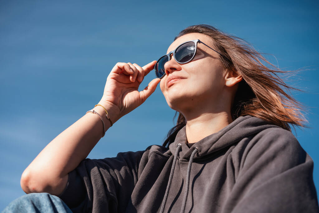 Портрет молодої дорослої жінки в сонцезахисних окулярах на блакитному небі
 - Фото, зображення
