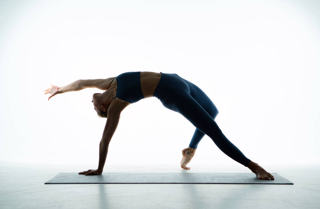 Flexibilní mladá fit dívka cvičit jógu provádět Wild Thing Pose pro strečink, wellness na bílém pozadí. Krásná baletka trénink na podlaze. Kvalitní fotografie - Fotografie, Obrázek